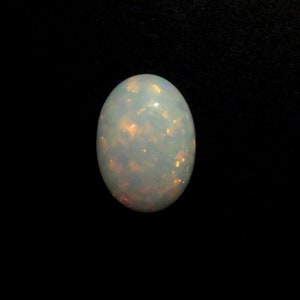 Peut inclure: Une pierre précieuse d'opale blanche avec une teinte bleu clair et des reflets orange et jaunes.