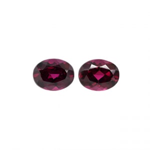 May include: Two oval-shaped gemstones, each a deep reddish-purple color. The gemstones are faceted and have a high polish.