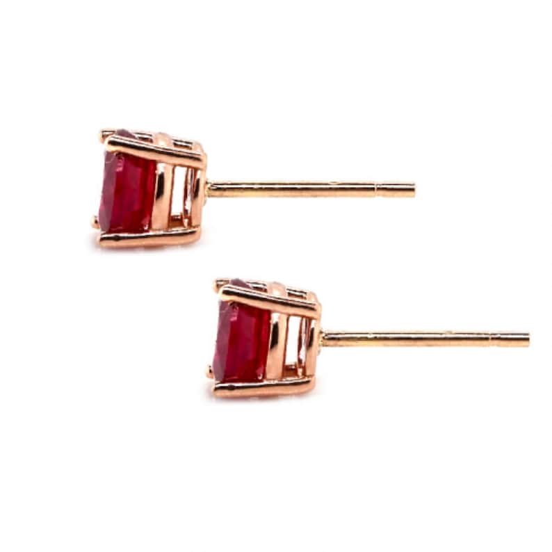 May include: A pair of rose gold stud earrings with a red ruby gemstone in each earring.