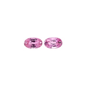 May include: Two oval-shaped pink gemstones, likely sapphires, are shown against a white background.