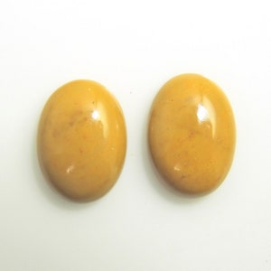 May include: Two oval-shaped, polished gemstones with a warm, golden-yellow hue. The stones have a smooth, glossy surface, reflecting light. The gemstones are set against a plain white background.