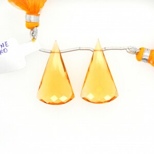 May include: Two orange faceted gemstone pendants on a silver chain. The pendants are triangular in shape and have a shiny, polished finish.