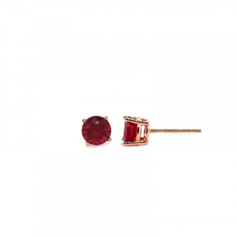May include: A pair of gold stud earrings with a red gemstone in the centre of each earring.
