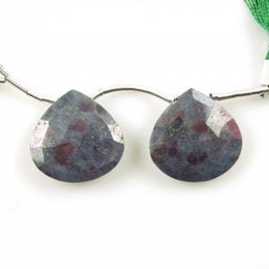 May include: Two pear-shaped gemstone beads with a dark blue and red speckled pattern. The beads are strung on a silver wire.