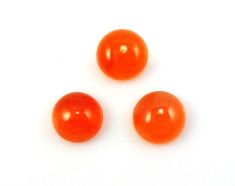 May include: Three round, polished, orange gemstones are arranged against a white background. The gemstones have a glossy finish, reflecting light. The gems are likely used for jewelry making or other crafts.