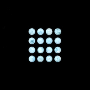 May include: A collection of 16 round, light blue gemstone cabochons arranged in a grid pattern.
