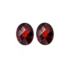 May include: Two oval-cut, faceted gemstones with a deep red color. The gemstones are displayed against a white background, showcasing their brilliance and clarity. These gems could be used for jewelry making.