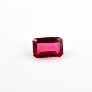 May include: A deep red gemstone with a rectangular emerald cut.