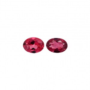 Puede incluir: Dos piedras preciosas rosadas de forma ovalada, cada una con un corte facetado.