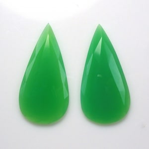 May include: Two pear-shaped green gemstones, likely chrysoprase, with a smooth, polished finish. The stones are displayed on a white background.