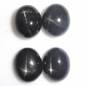 Könnte beinhalten: Vier schwarze sternförmige Cabochon-Edelsteine. Die Steine sind oval geformt und haben einen silbrigen Schimmer.