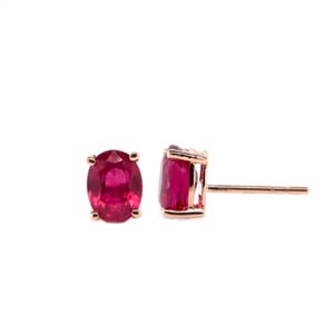 May include: A pair of rose gold stud earrings with oval-shaped ruby gemstones.