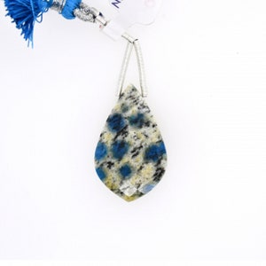 Pode incluir: Um pingente em forma de lágrima com uma pedra salpicada de azul e branco. A pedra está engastada em uma configuração de prata.