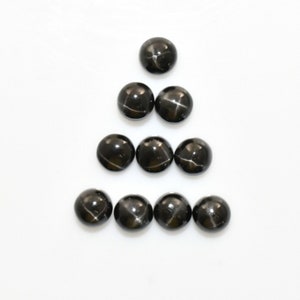 Könnte beinhalten: Neun schwarze Stern-Cabochons, die in Pyramidenform angeordnet sind. Die Steine haben ein sternförmiges Muster in der Mitte.
