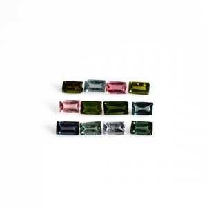 May include: Assortment of green, blue, and pink gemstones in rectangular shapes. The gemstones are arranged in three rows on a white background.