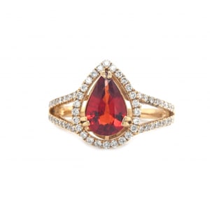 Könnte beinhalten: Ein Ring mit einem roten, birnenförmigen Edelstein und einem Halo aus kleinen Diamanten, gefasst in Gold.