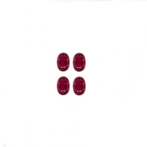 Puede incluir: Cuatro piedras preciosas ovaladas de color rojo oscuro. Las piedras preciosas están dispuestas en una cuadrícula de dos por dos.