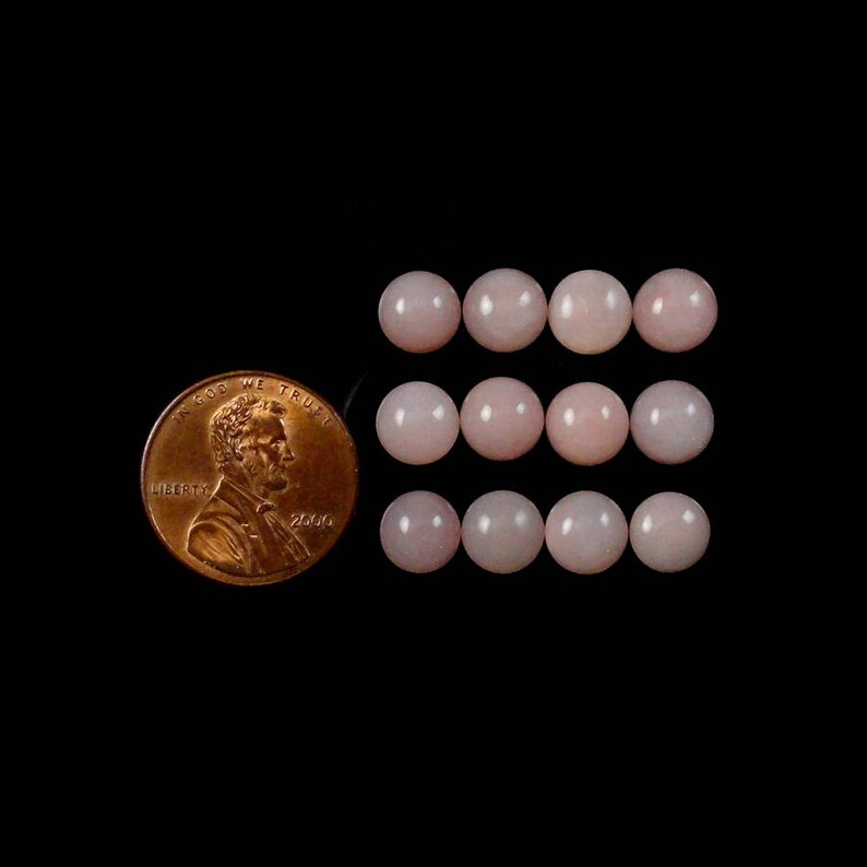 K&ouml;nnte beinhalten: Eine Sammlung von 12 rosafarbenen Opal-Cabochons, jeder etwa so gro&szlig; wie ein 1-Cent-St&uuml;ck.