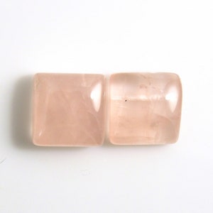 May include: Two square-shaped, pale pink rose quartz cabochons. The stones are smooth and polished.