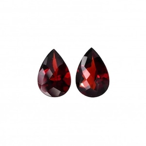 May include: Two pear-shaped red gemstones, likely garnets, with a faceted cut.