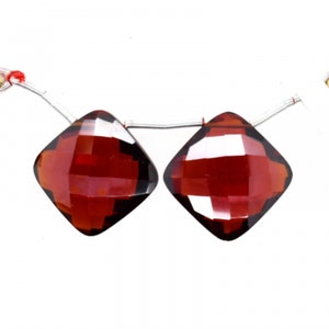 May include: Two red gemstone beads with a faceted square shape. The beads are strung on a silver wire.