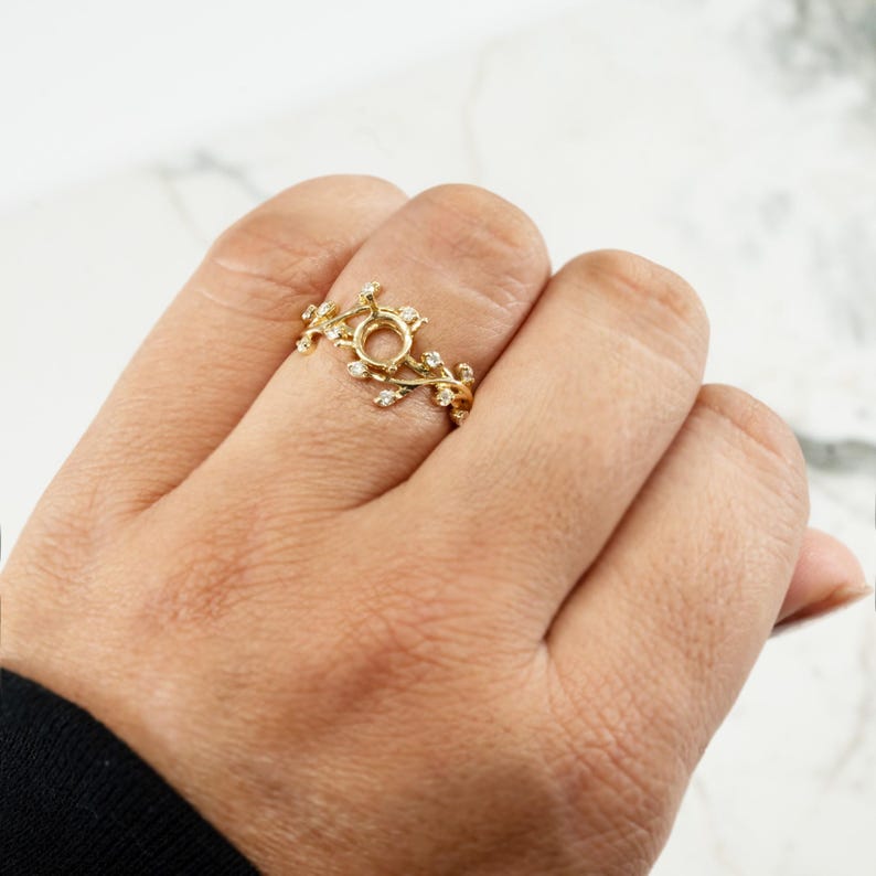 Puede incluir: Un anillo de oro con un delicado dise&ntilde;o de vid y peque&ntilde;as piedras transparentes. El anillo tiene un engaste central redondo para una piedra.