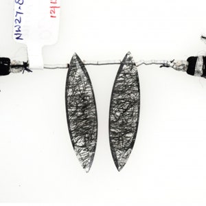 May include: Two clear quartz crystal pendants with black inclusions, strung on a silver wire. The pendants are oval shaped and have a pointed tip. The text "NW27-8 MM" and "121" are visible on a white label.