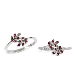 May include: Two silver rings with a delicate design of intertwined branches adorned with small red gemstones.