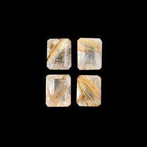 Pode incluir: Quatro pedras preciosas retangulares com base transparente e inclusões douradas, sobre fundo preto. As pedras são cortadas com uma borda facetada, e as inclusões douradas criam um efeito visual marcante.