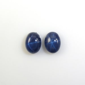 May include: Two blue star sapphire cabochons, each with a six-pointed star in the center.