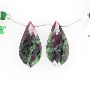 May include: Two teardrop-shaped green, pink, and black gemstone beads. The beads are faceted and have a pearlescent sheen.