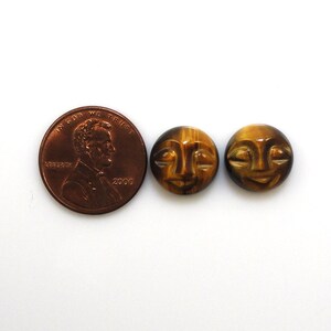 May include: Two brown tiger's eye cabochons with carved faces. The cabochons are about the size of a US penny.