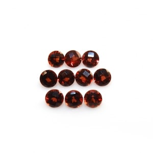May include: Ten round, faceted, red gemstones. The gemstones are arranged in a staggered pattern on a white background.