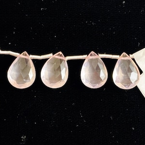 May include: Four pink teardrop-shaped gemstone beads strung on a silver wire.