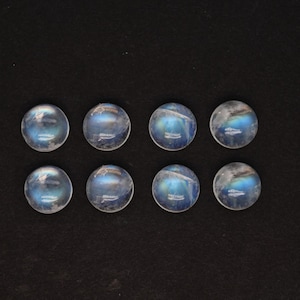May include: Eight round, iridescent moonstone cabochons with a blue sheen. The stones are arranged in two rows of four.