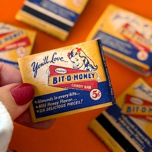 May include: Vintage Bit-O-Honey candy bar wrappers. The wrappers are yellow, red, and blue, with the text "You'll Love..." and "BIT-O-HONEY CANDY BAR." The wrappers also state "Almonds in every bite... Mild Honey Flavor... SIX DELICIOUS PIECES!"