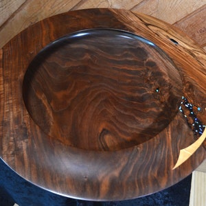 May include: A large, dark brown wooden bowl with a wide rim. The bowl has a natural wood finish and a unique inlay of blue and gold accents.