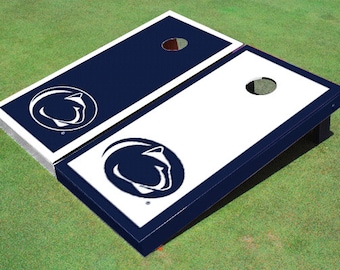 May include: A white and blue cornhole set with the Penn State Nittany Lions logo. The set includes two boards with a blue frame and a white playing surface. The logo is a white lion's head inside a blue circle.
