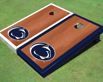 May include: Two wooden cornhole boards with a navy blue trim and a white Penn State Nittany Lion logo. The boards are set up on a green grassy surface.