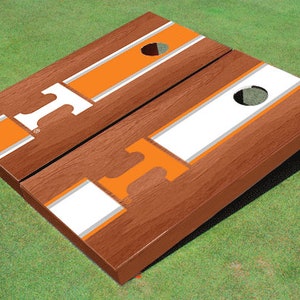 May include: A set of two wooden cornhole boards with a white and orange striped design. The boards feature a large orange letter "T" on each side.