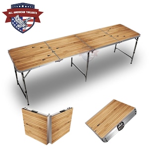 May include: A wooden folding table with a wood grain design and a silver frame. The table is folded up and has a carrying handle. The table is labeled "All American Tailgate".