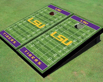 Puede incluir: Un juego de dos tablas de cornhole de tamaño reglamentario con un diseño personalizado de LSU Tigers. Las tablas presentan un campo de fútbol verde y blanco con el logotipo de LSU y las palabras "LSU" y "TIGERS" en morado y dorado.