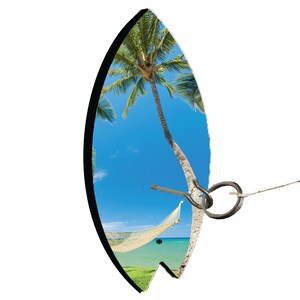 May include: A wooden surfboard with a tropical beach scene printed on it. The surfboard has a hammock hanging from it and a metal ring attached to the side.