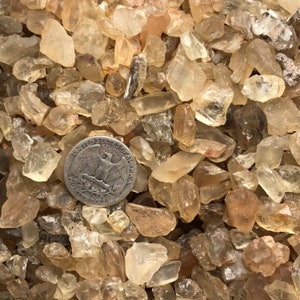 May include: A close-up of a pile of small, translucent, light brown sunstone crystals. A US quarter is included for scale.