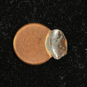 May include: A copper penny with a large piece of silver tape covering half of the coin.