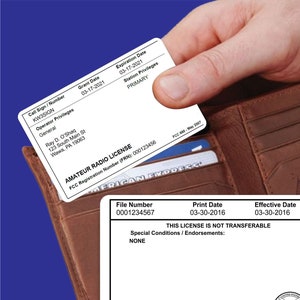 May include: A close-up of a brown leather wallet with a white card inside. The card is an amateur radio license with the FCC registration number 000123456. The card shows the license holder's name, call sign, grant date, expiration date, and station privileges. The card also includes the text "This license is not transferable."