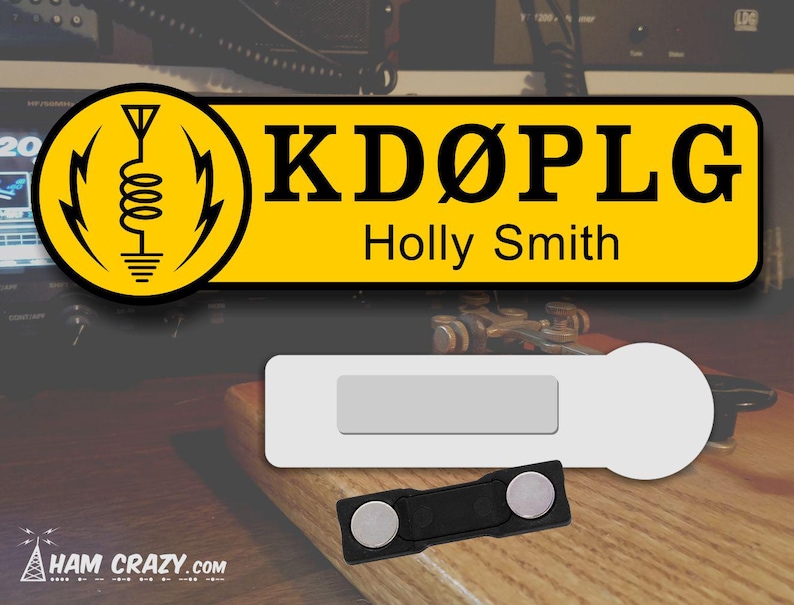 May include: A yellow name tag with a black antenna symbol and the text "KD&Oslash;PLG Holly Smith". The name tag is attached to a white magnetic name tag holder with a black magnetic clasp.