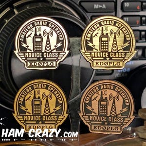 Puede incluir: Cuatro insignias circulares de metal dorado con un gráfico de radio, antena y satélite. El texto dice AMATEUR RADIO OPERATOR, NOVICE CLASS y KDØPLG. Las insignias están dispuestas en una cuadrícula sobre un fondo de equipo de radio.