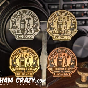 May include: Four circular metal badges in silver, gold, brass, and copper finishes. Each badge features an engraved design of a handheld radio, a transmission tower, and lightning bolts. Text reads AMATEUR RADIO OPERATOR, TECHNICIAN CLASS, and KDØPLG.