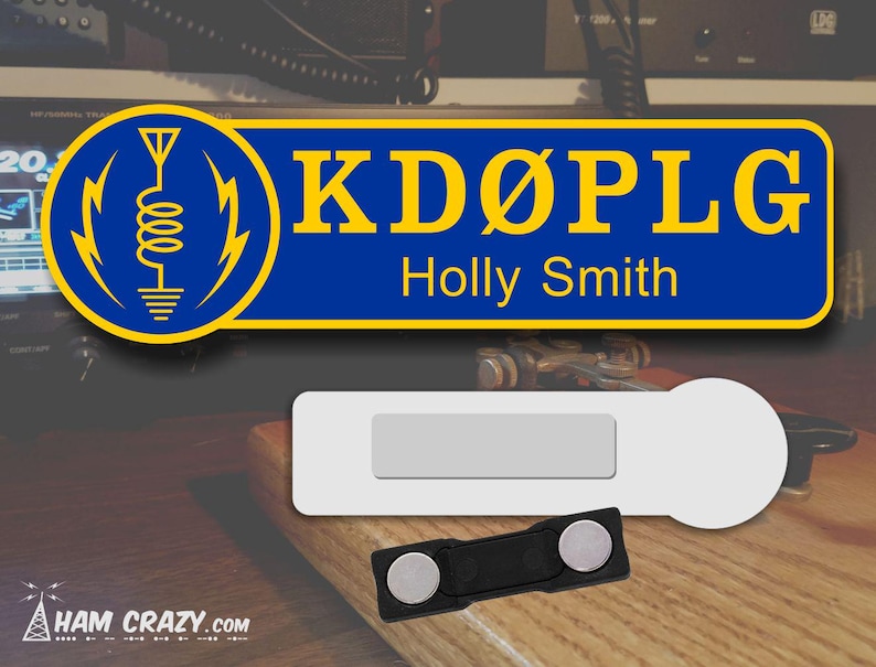 May include: A blue and yellow name tag with the call sign "KD&Oslash;PLG" and the name "Holly Smith" printed on it. The name tag is attached to a magnetic backing.